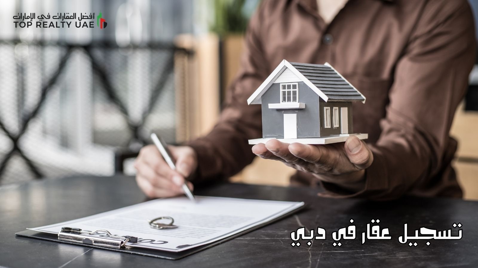 تسجيل عقار في دبي مع نموذج لعقد عقاري وصورة لمنزل صغير في يد شخص.